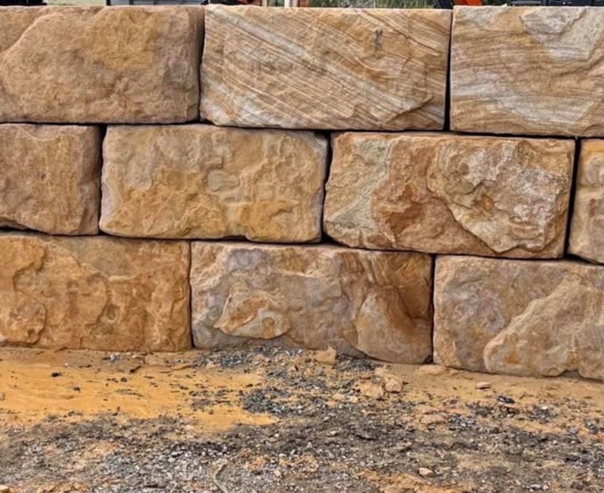 Close-up of stacked tan and brown stone or brick wall with sandy ground at base