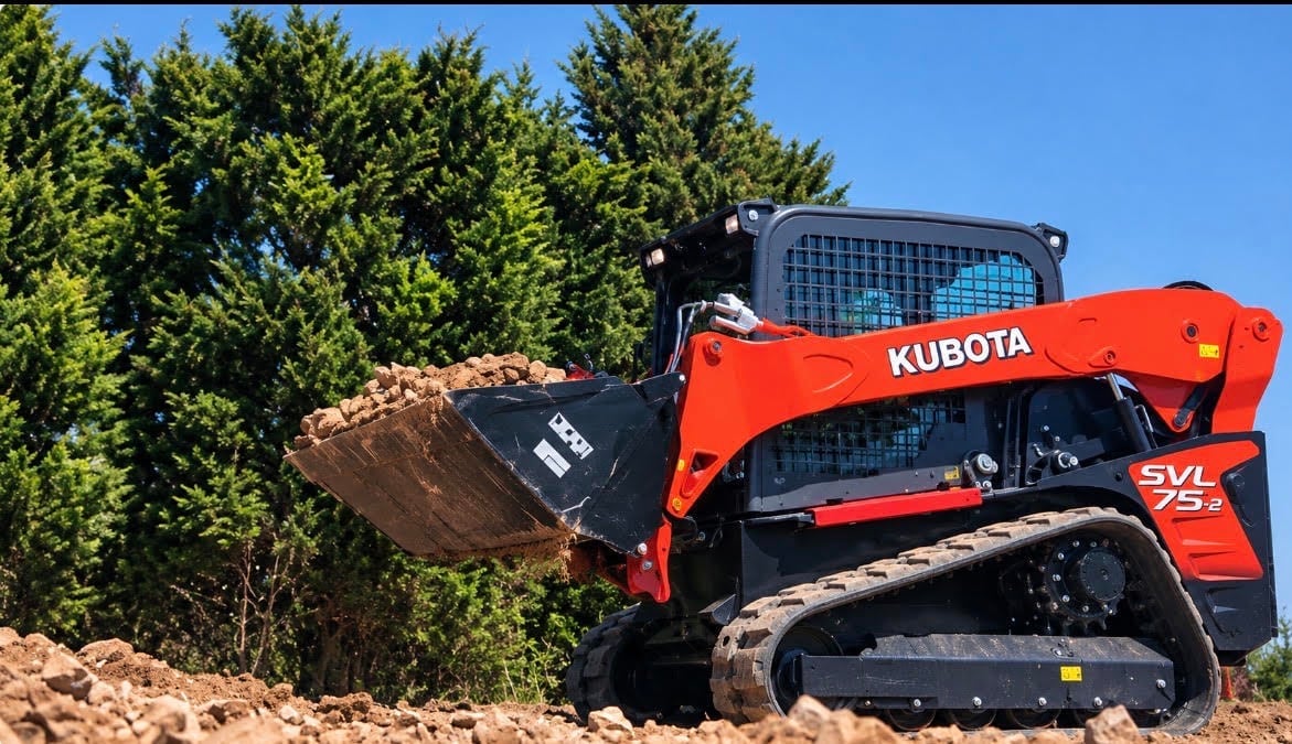 Red Kubota skid steer loader with bucket attachment filled with dirt, parked outdoors with green trees in background