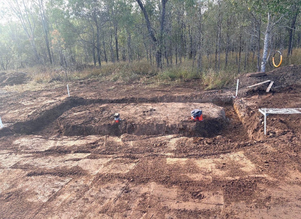 Worker digging in sandy pit surrounded by forest trees and wooden markers