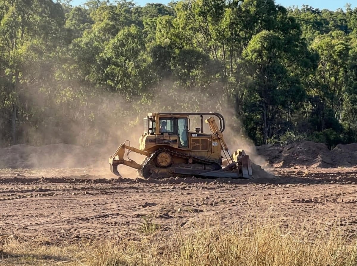 Bulldozer clearing land with dust clouds, surrounded by dense green forest vegetation in background